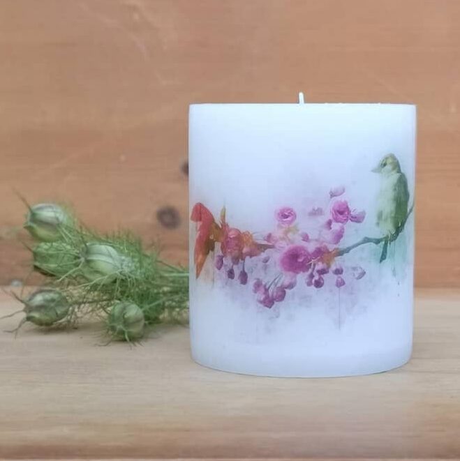 Candle with picture of bird on blossom branch.