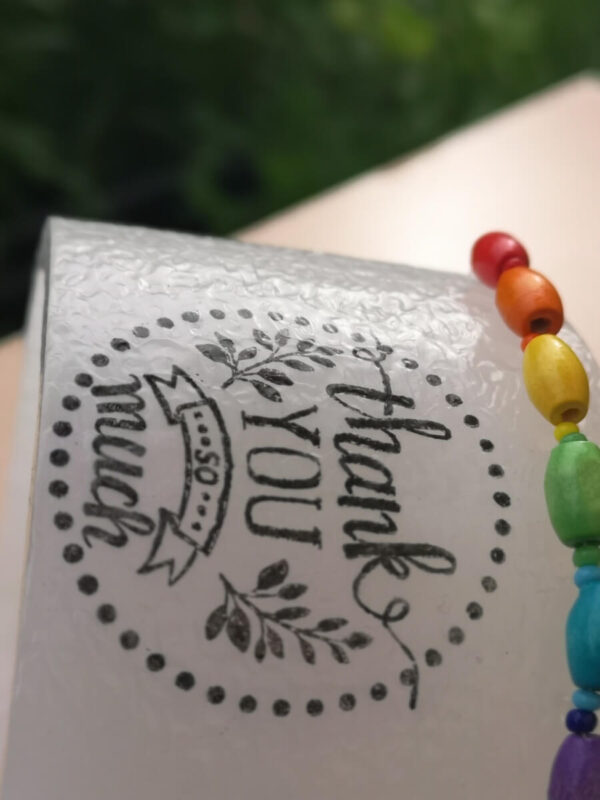 Small wax lantern decorated with coloured wooden beads and 'thank you' print on it.
